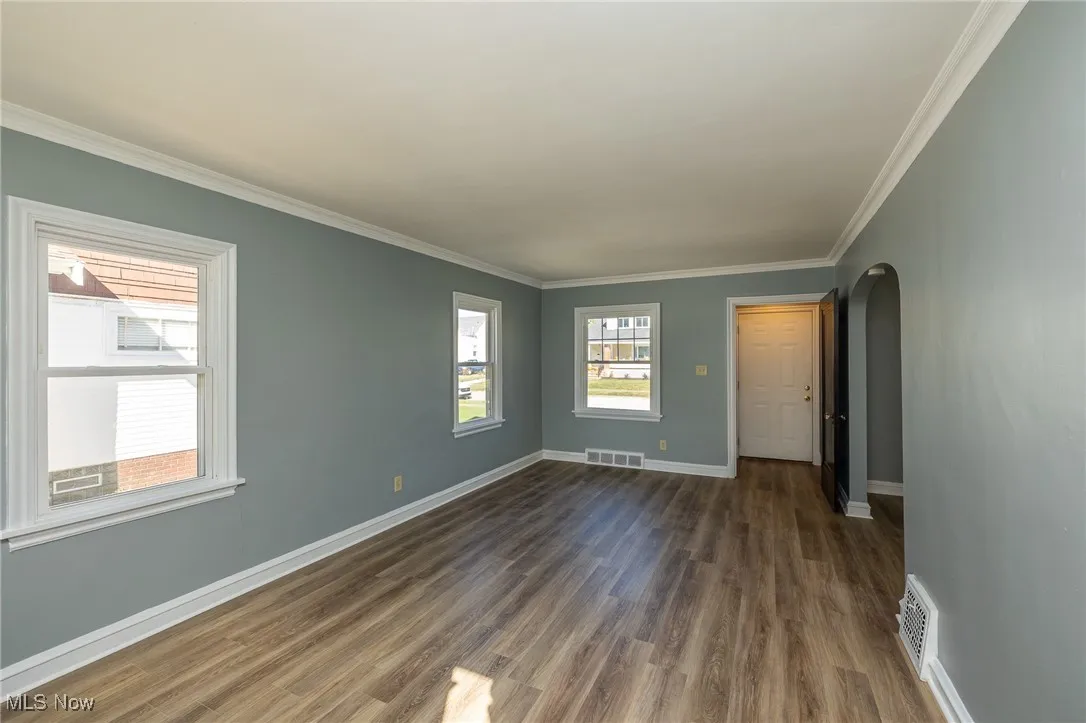 Spare room with arched walkways, ornamental molding, and wood finished floors