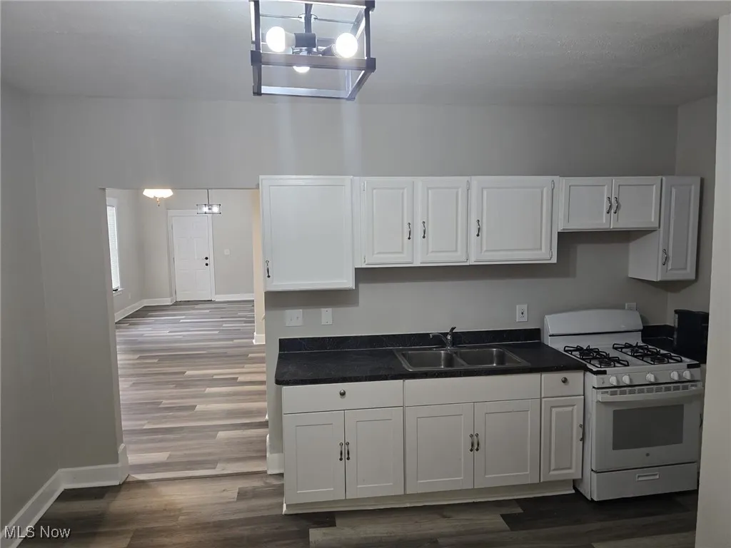 Kitchen with white gas range oven, dark countertops, white cabinetry, and dark wood-type flooring