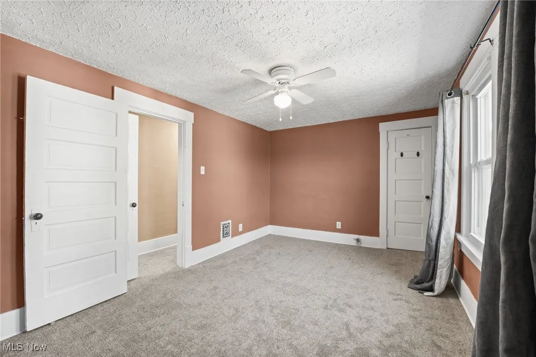 Unfurnished room featuring light carpet, ceiling fan, and a textured ceiling