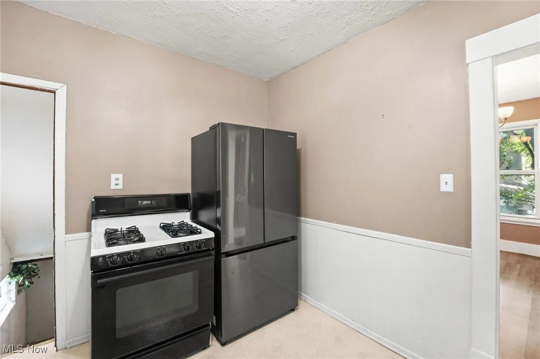 Kitchen featuring gas stove, freestanding refrigerator, a wainscoted wall, a textured ceiling, and a chandelier
