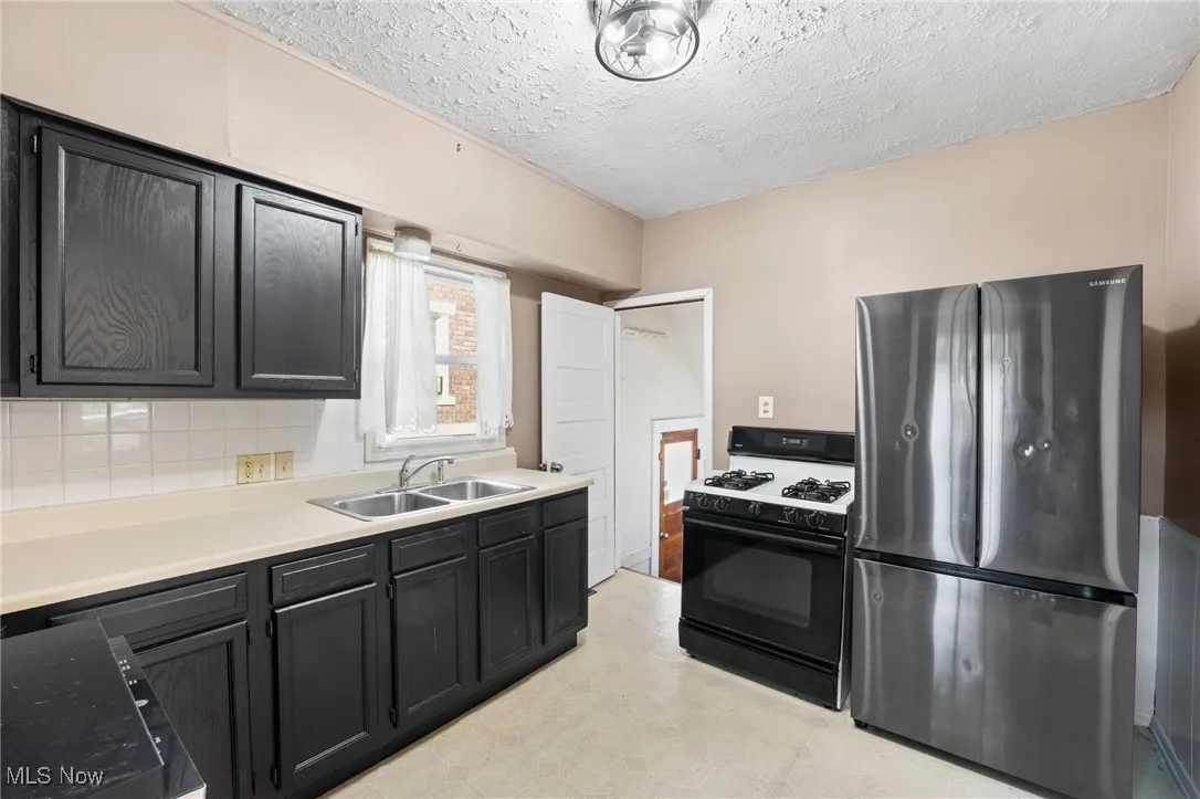 Kitchen featuring freestanding refrigerator, gas stove, light countertops, a textured ceiling, and light flooring
