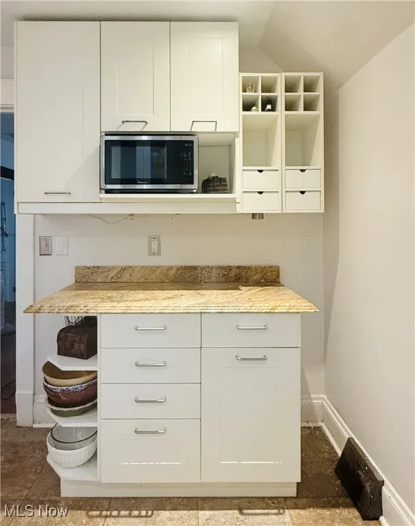 Kitchen featuring open shelves, white cabinets, stainless steel microwave, and light stone countertops