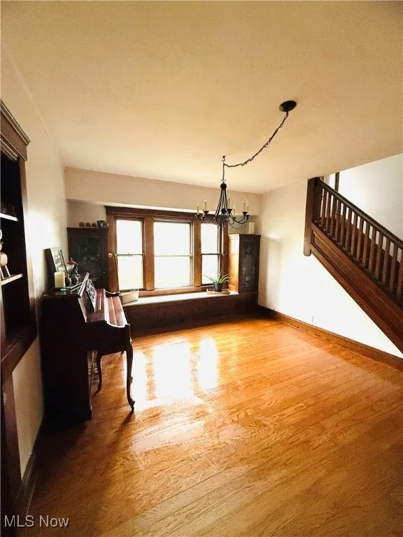 Unfurnished living room with light wood-style floors, a chandelier, and stairs