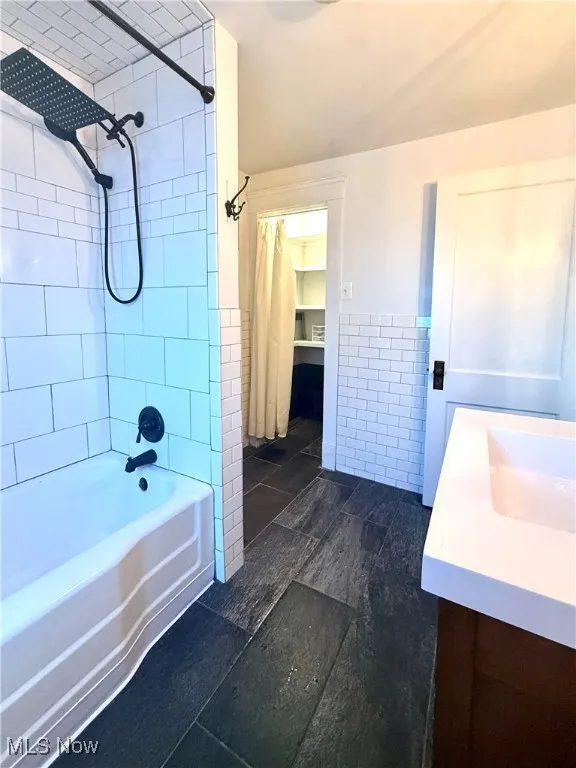 Bathroom featuring tile walls, vanity, shower / bath combo, and wainscoting