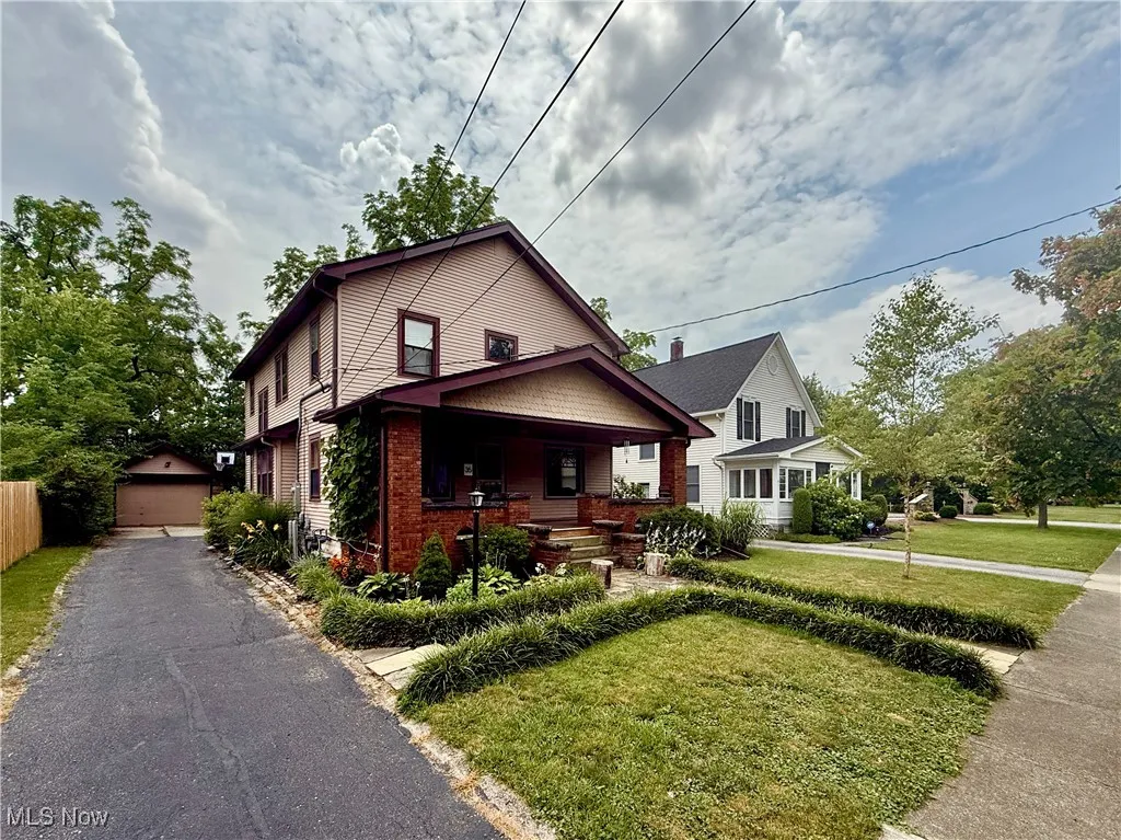 View of front of home featuring covered porch, a front yard, a detached garage, brick siding, and an outbuilding