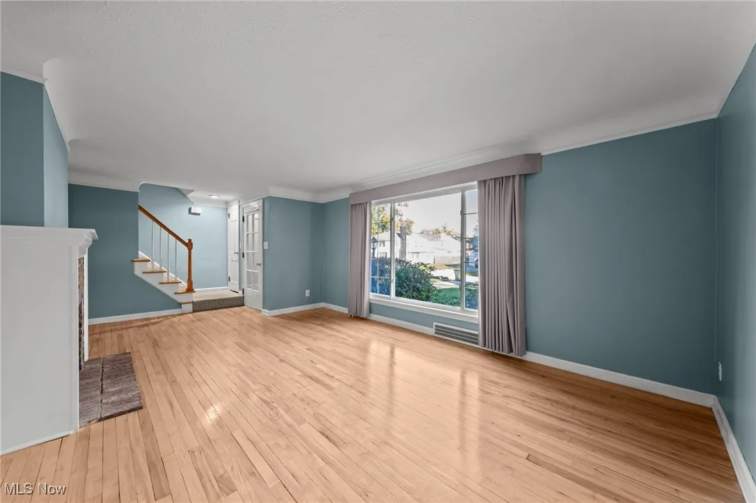 Unfurnished living room featuring stairway, light wood finished floors, and crown molding