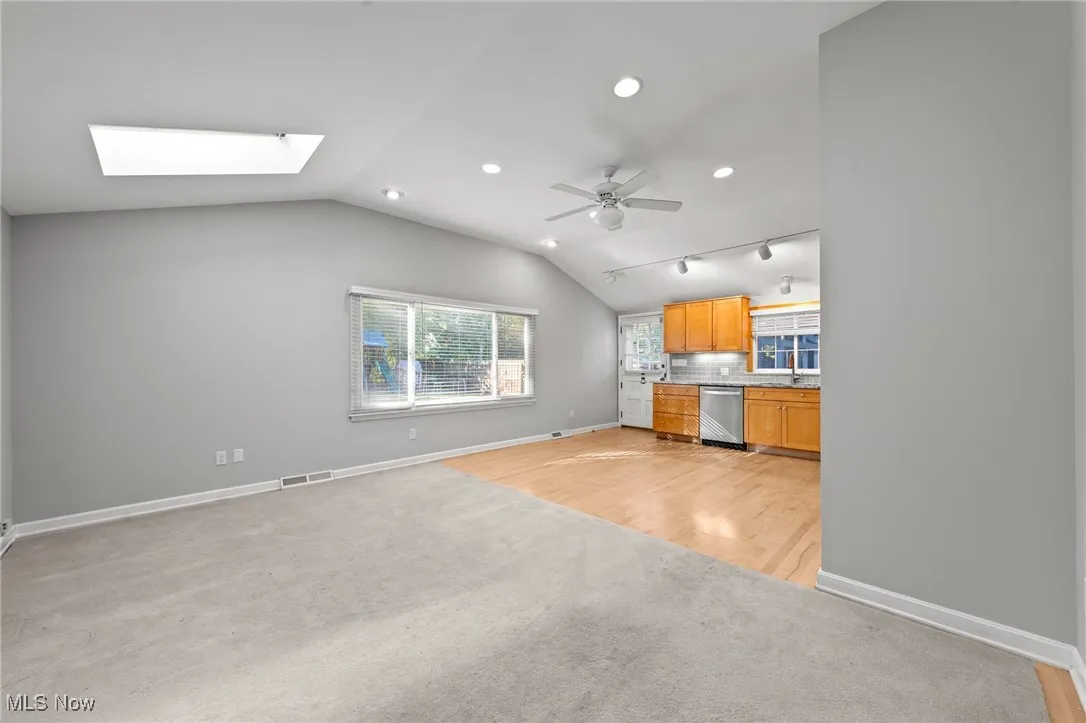 Kitchen featuring light wood-type flooring, lofted ceiling, stainless steel dishwasher, light carpet, and decorative backsplash