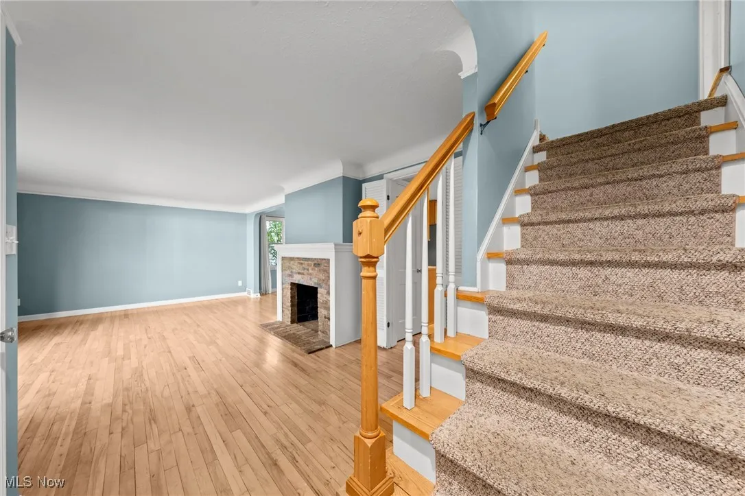 Stairs featuring wood-type flooring, a brick fireplace, and crown molding