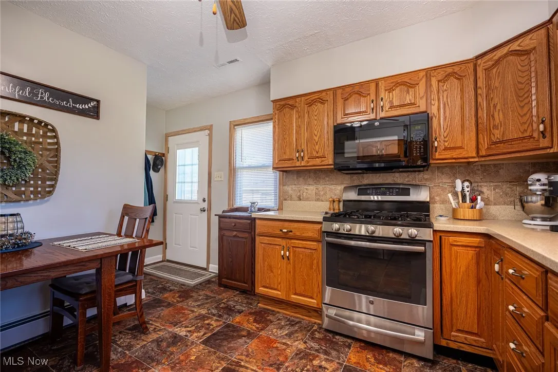 Kitchen with brown cabinets, stainless steel range with gas stovetop, black microwave, a textured ceiling, and backsplash