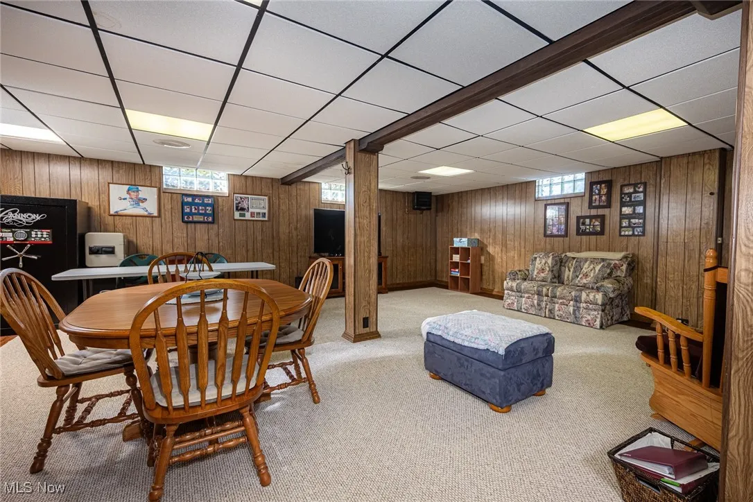 Dining room with plenty of natural light, carpet flooring, wood walls, and a paneled​​‌​​​​‌​​‌‌​‌‌​​​‌‌​‌​‌​‌​​​‌​​ ceiling