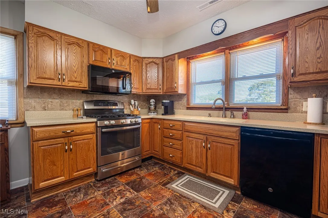 Kitchen with brown cabinets, healthy amount of natural light, backsplash, black appliances, and a textured ceiling