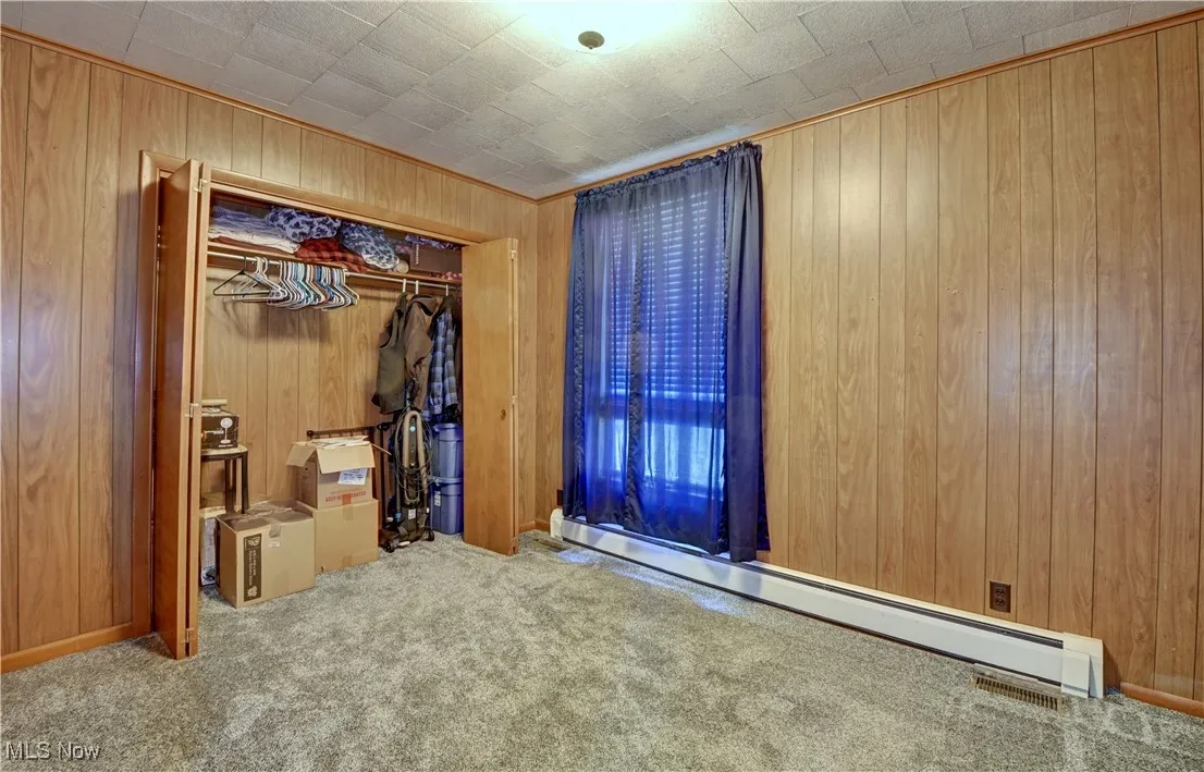 Unfurnished bedroom featuring a baseboard heating unit, wooden walls, carpet, and a closet
