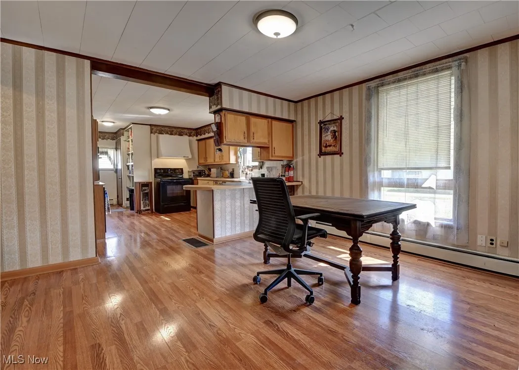 Office area featuring wallpapered walls, light wood-style floors, baseboard heating, and ornamental molding