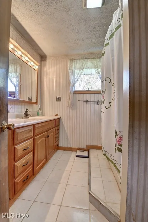 Full bath featuring light tile patterned floors, a textured ceiling, vanity, a shower with shower curtain, and wallpapered walls