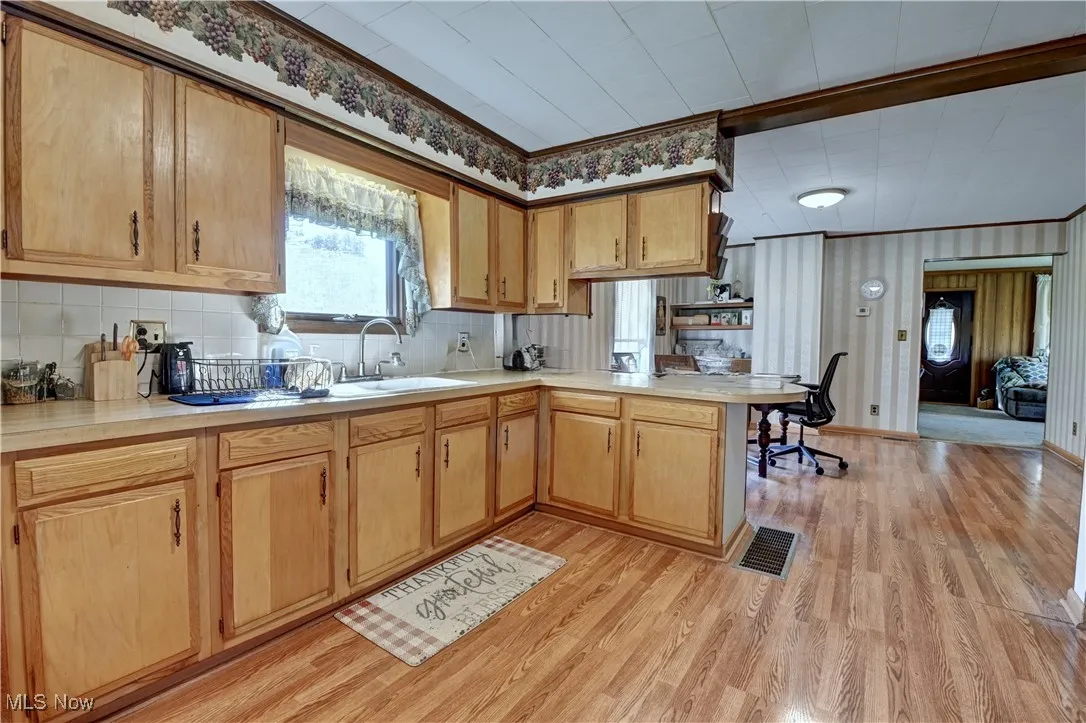 Kitchen with a peninsula, light countertops, light wood-style flooring, and tasteful backsplash