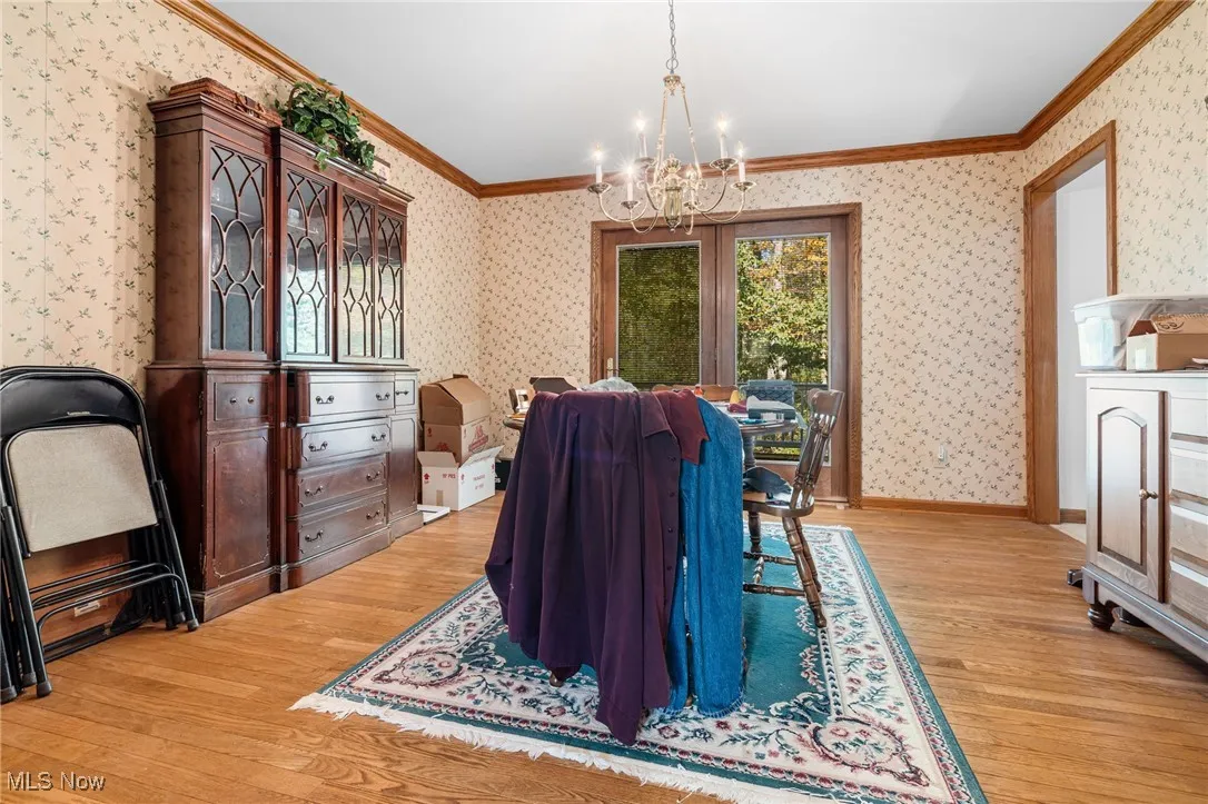 Dining room featuring crown molding, light wood-style flooring, a chandelier, and wallpapered walls