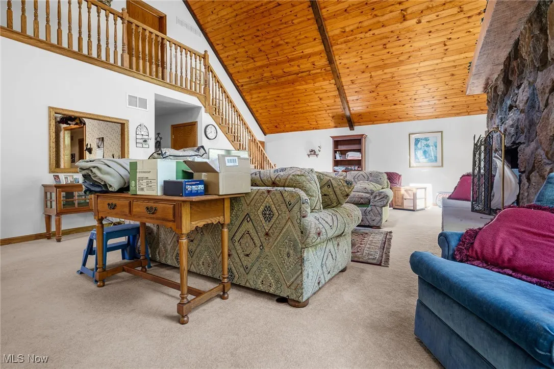 Carpeted living room featuring stairway, high vaulted ceiling, and a wooden ceiling with exposed beams