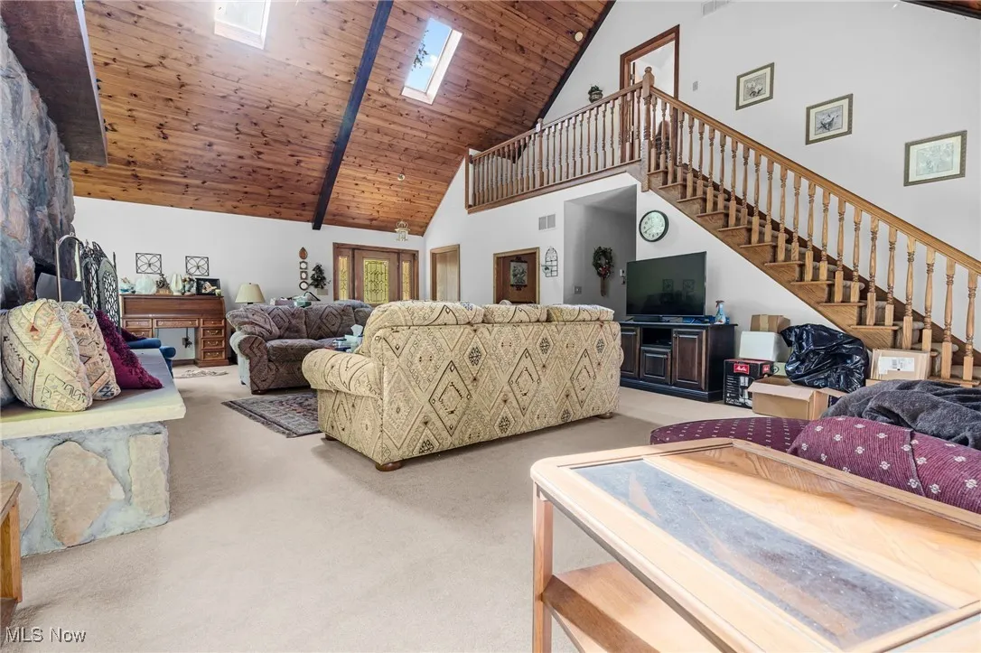 Living room with a skylight, light carpet, high vaulted ceiling, a wood ceiling with exposed beams, and stairway