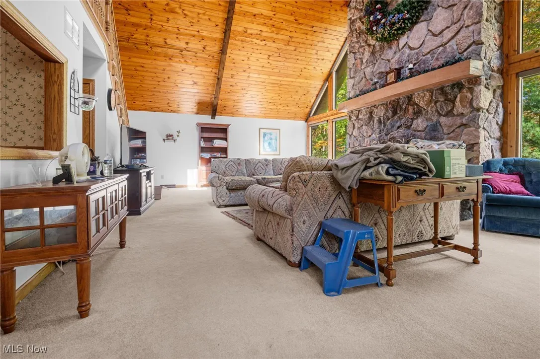 Living room featuring a wood ceiling with exposed beams, light carpet, plenty of natural light, and high vaulted ceiling