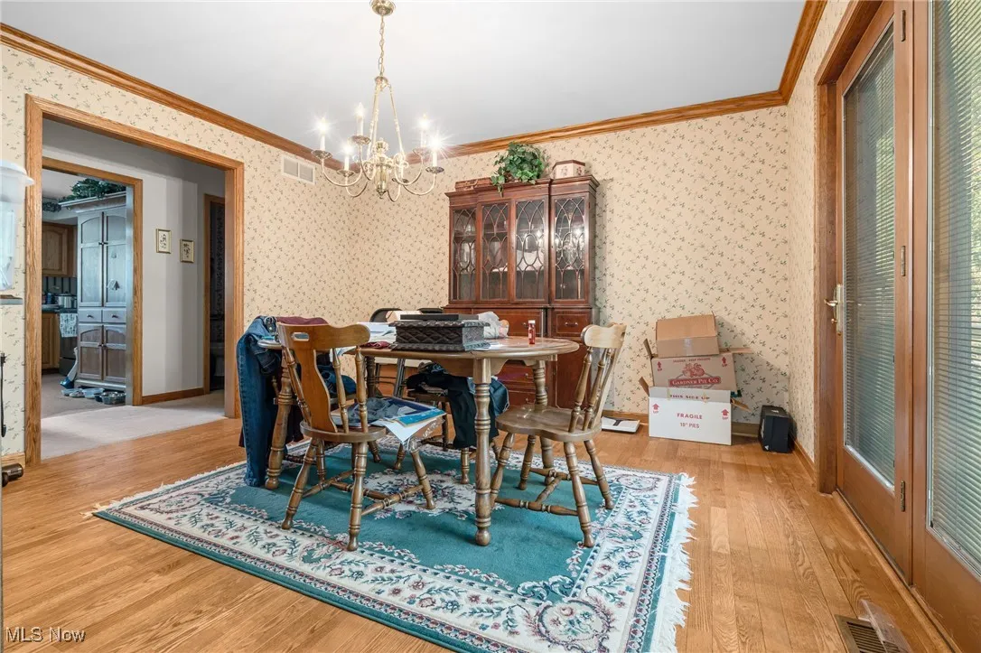 Dining room featuring wallpapered walls, crown molding, light wood-style floors, and a chandelier