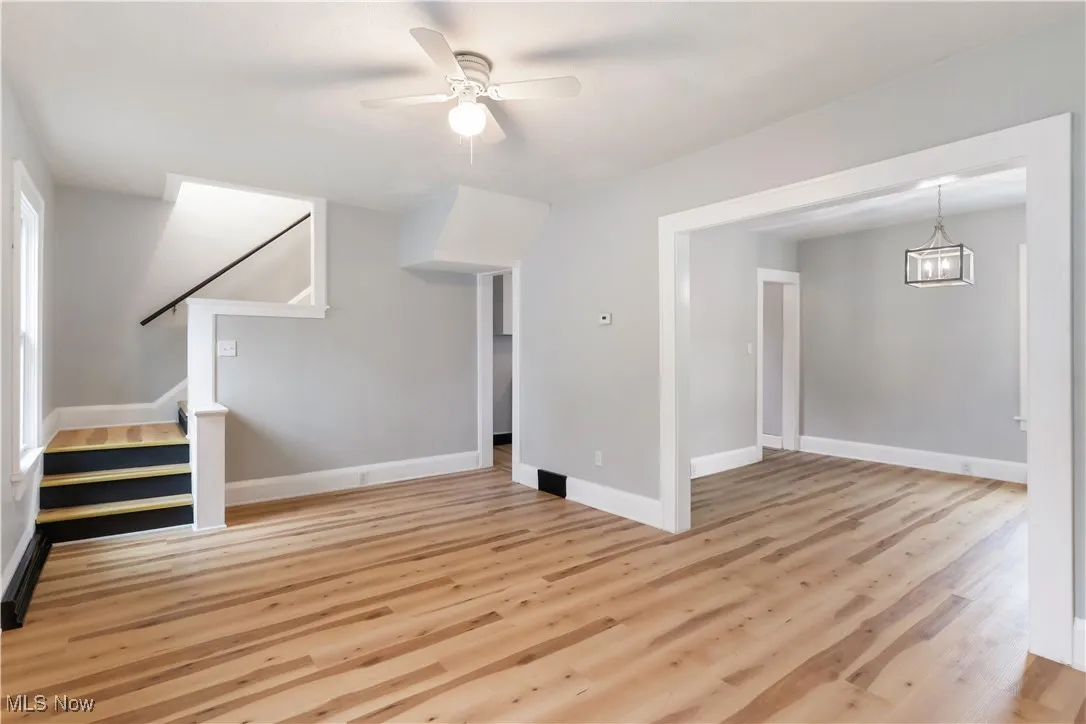 Unfurnished living room featuring light wood-style floors, stairway, ceiling fan, a chandelier, and plenty of natural light