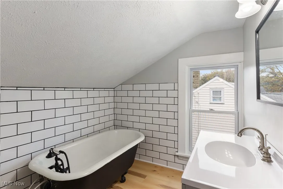 Bathroom featuring vanity, a textured ceiling, light wood-style floors, a soaking tub, and tile walls