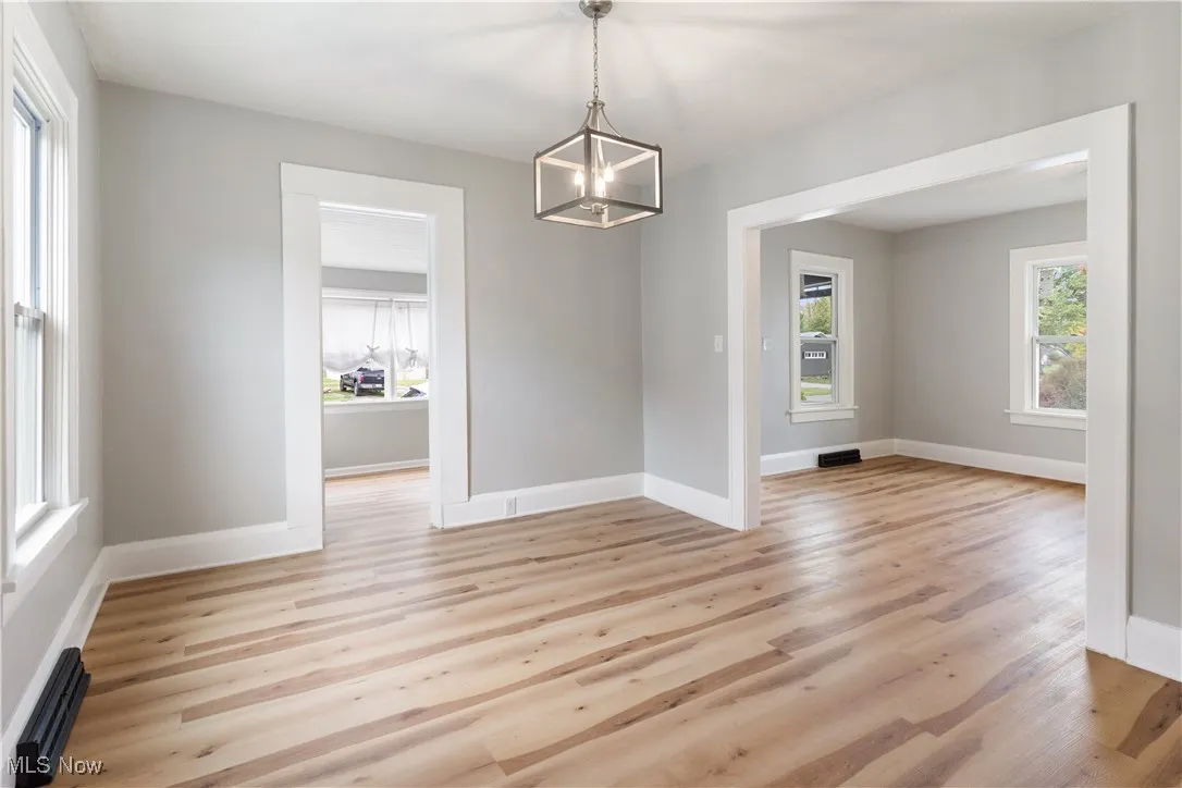 Unfurnished dining area featuring light wood finished floors, a baseboard radiator, and a chandelier