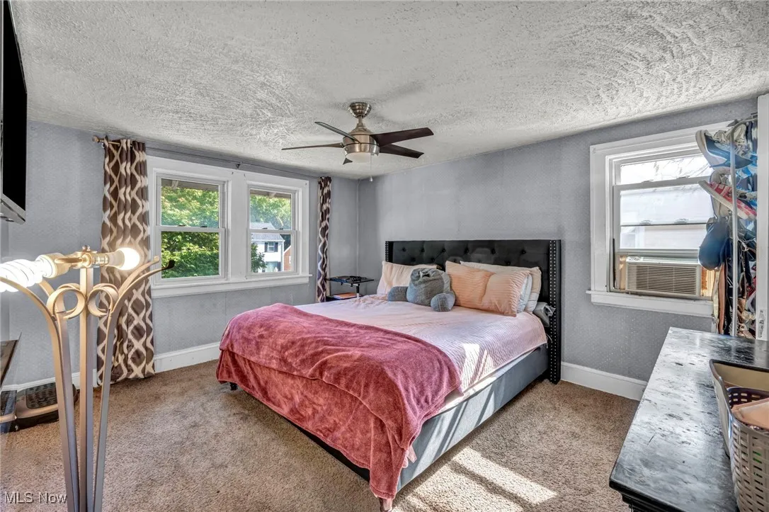 Bedroom with carpet floors, multiple windows, a ceiling fan, and a textured ceiling