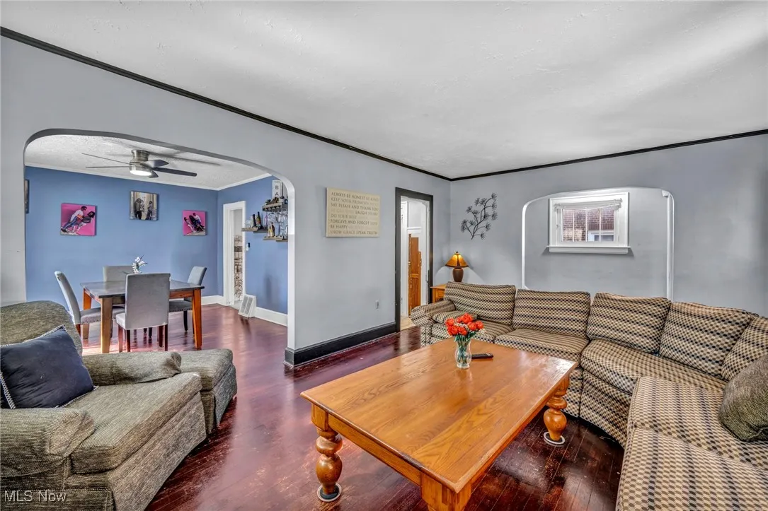 Living room featuring arched walkways, a ceiling fan, wood finished floors, crown molding, and a textured ceiling