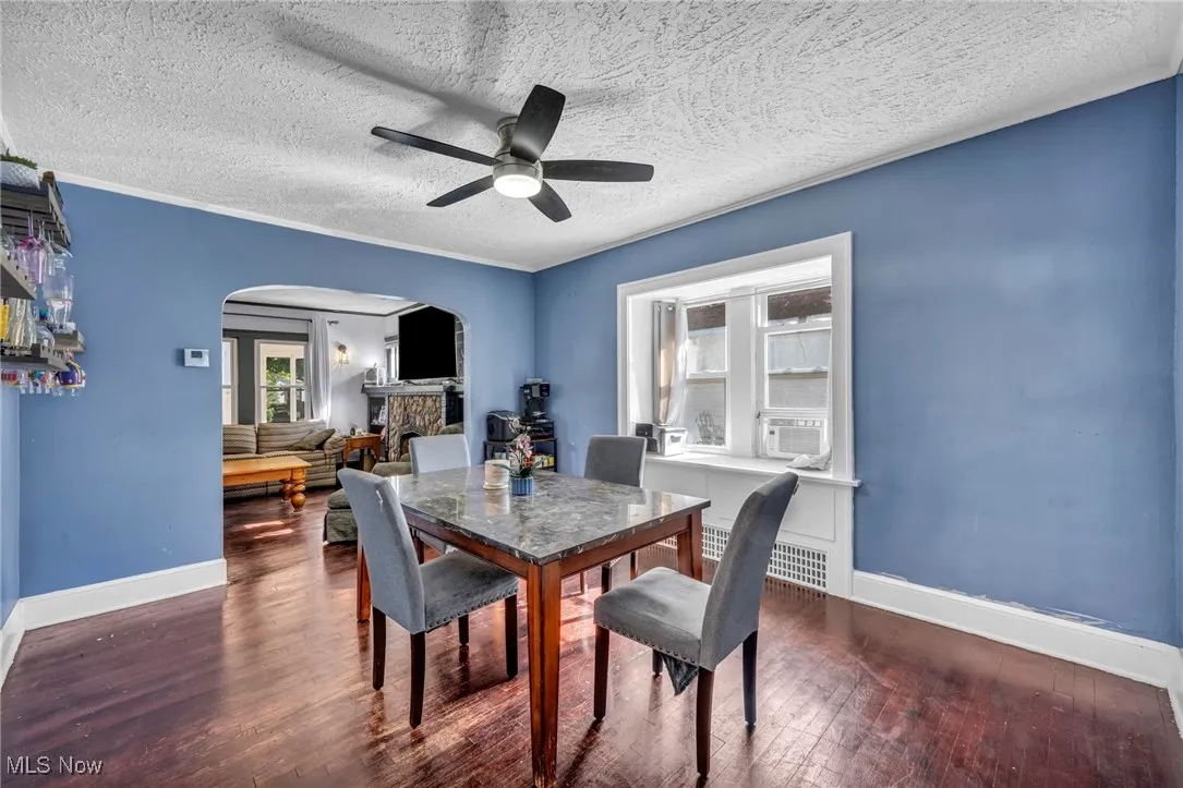 Dining room featuring arched walkways, dark wood-style floors, a textured ceiling, ceiling fan, and ornamental molding