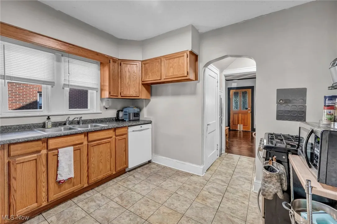 Kitchen with arched walkways, dishwasher, black microwave, brown cabinets, and dark countertops