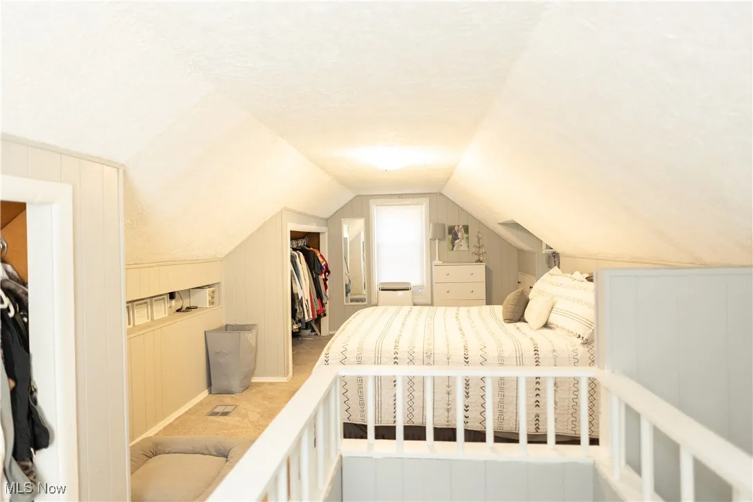 Carpeted bedroom with a spacious closet, vaulted ceiling, and a textured ceiling