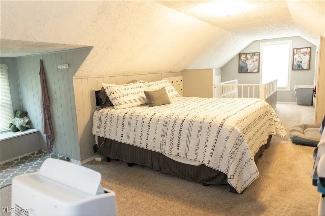 Bedroom featuring a textured ceiling, light carpet, wooden walls, and vaulted ceiling