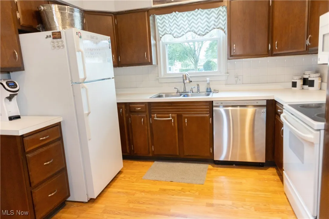 Kitchen with white appliances, light countertops, light wood-style floors, and backsplash