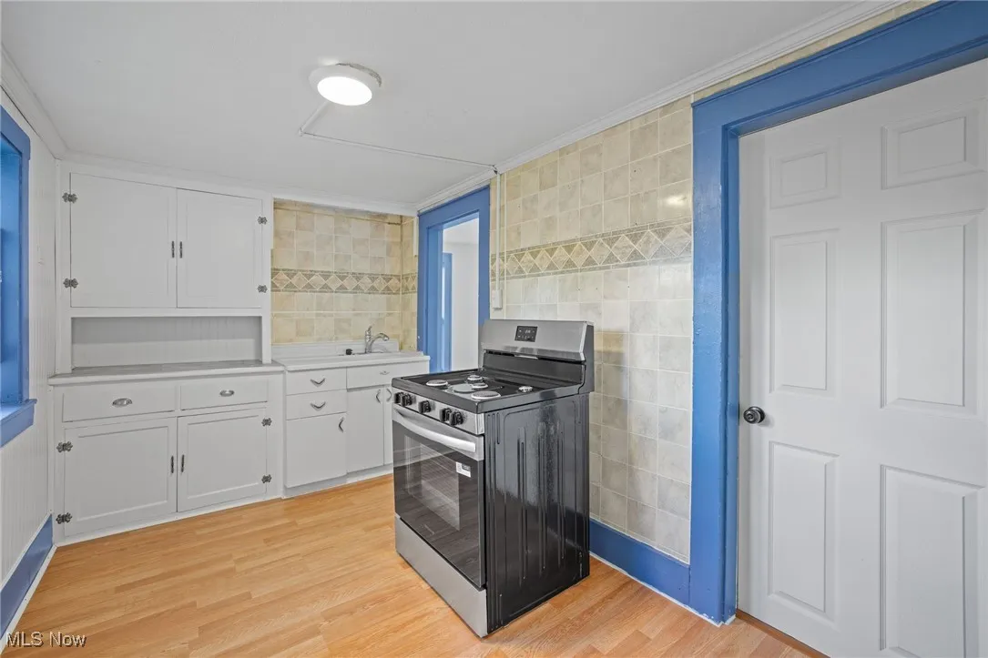 Kitchen with stainless steel gas range oven, tile walls, light wood-style flooring, white cabinetry, and light countertops