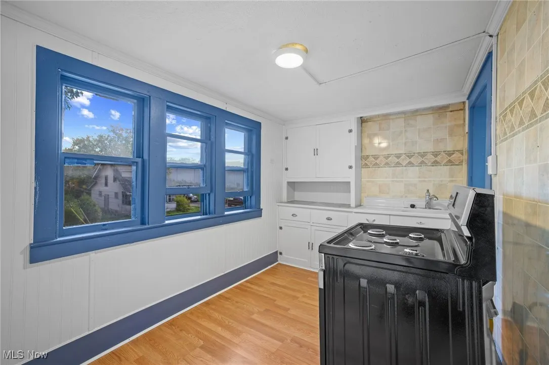Kitchen featuring freestanding range oven, light wood-style flooring, crown molding, light countertops, and white cabinetry