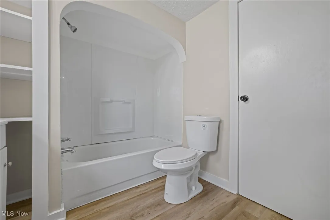 Full bathroom with light wood-type flooring, shower / tub combination, and a textured ceiling