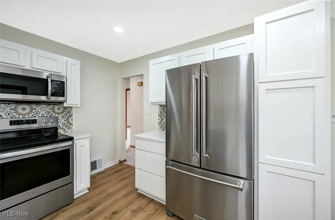 Kitchen featuring appliances with stainless steel finishes, white cabinetry, light wood-style flooring, backsplash, and recessed lighting