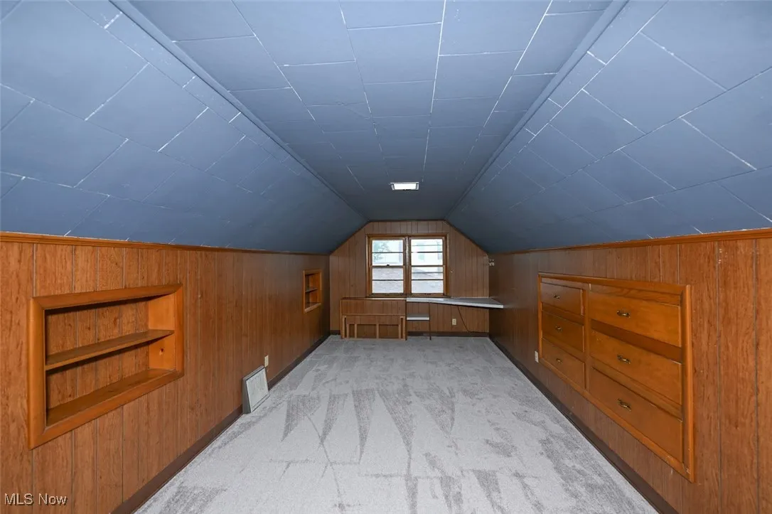 Additional living space featuring lofted ceiling, built in features, wood walls, and light carpet