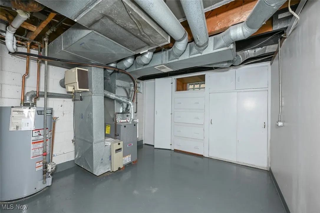 Unfinished below grade area with gas water heater, heating unit, and concrete block wall