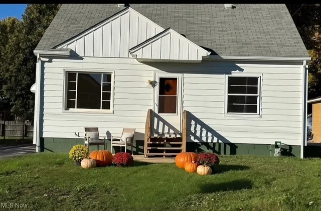 Rear view of house with a shingled roof, a yard, and entry steps