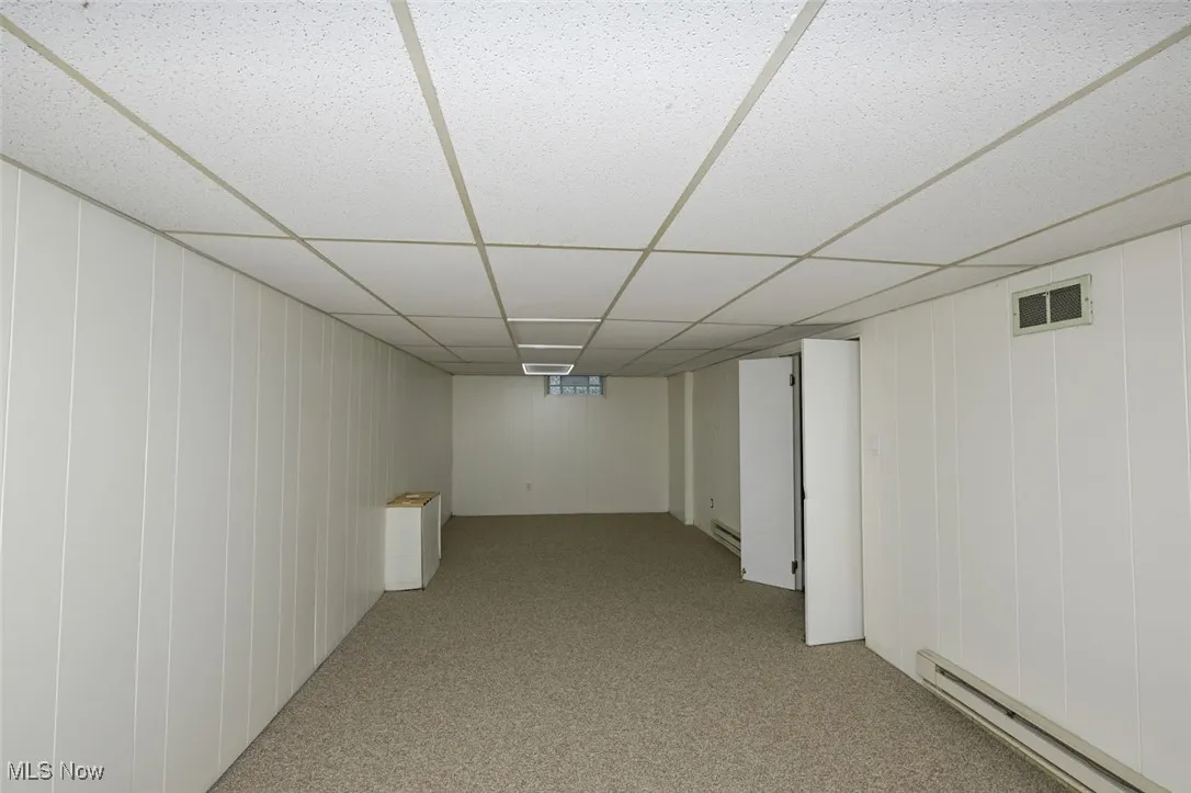 Finished below grade area featuring a baseboard heating unit, light carpet, and a paneled ceiling