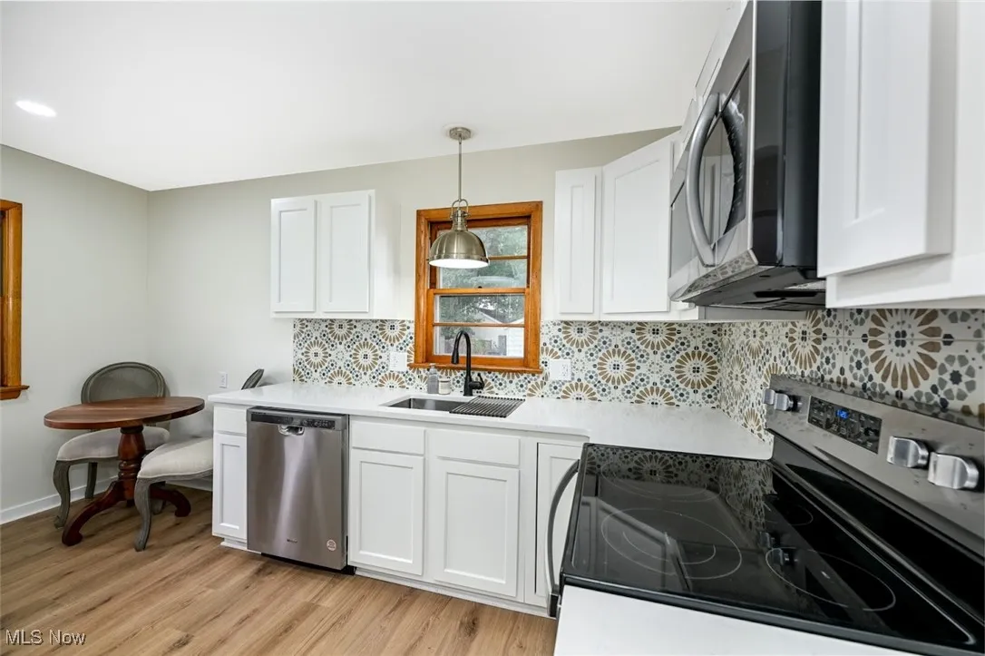 Kitchen featuring appliances with stainless steel finishes, white cabinetry, light wood-style flooring, and backsplash