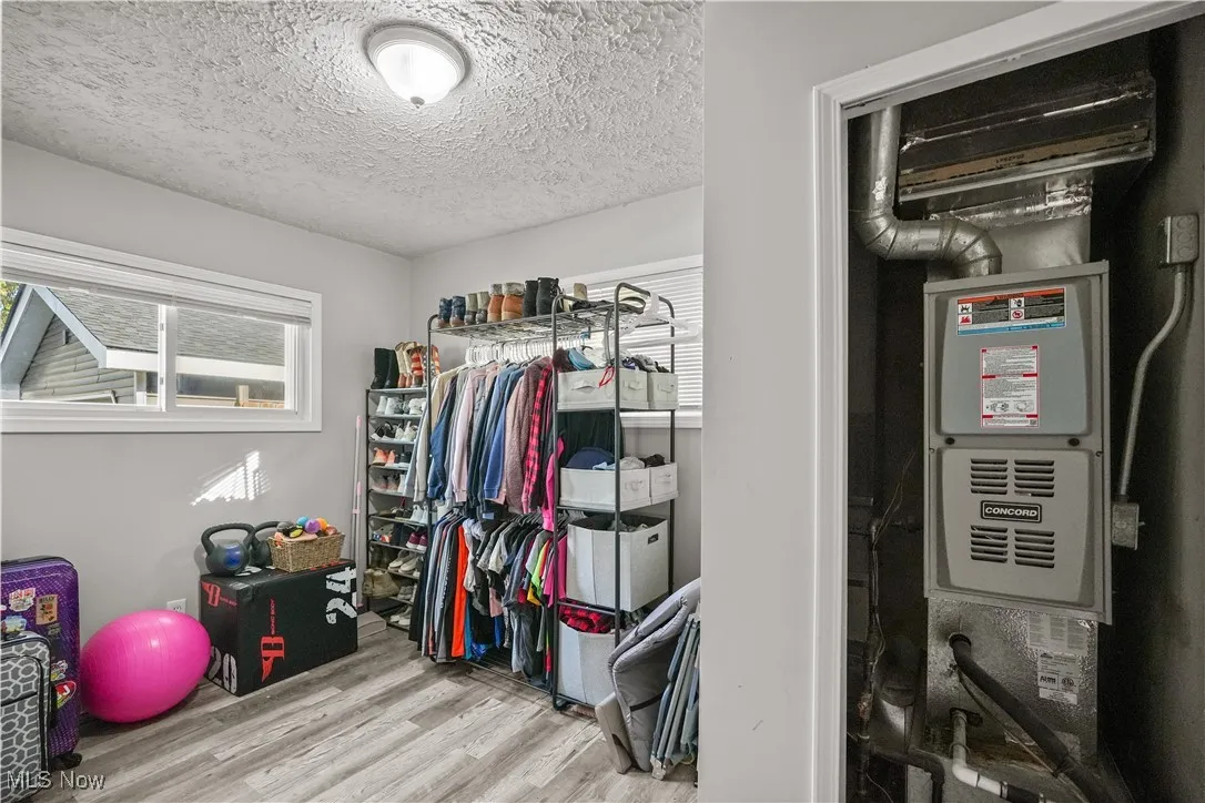 Walk in closet with light wood finished floors and heating unit
