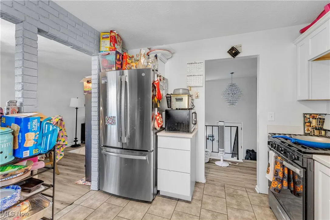 Kitchen with white cabinets, freestanding refrigerator, range with gas stovetop, light countertops, and light tile patterned floors