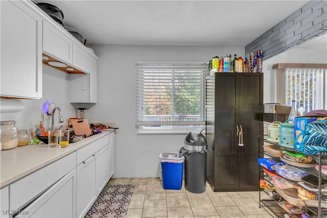 Kitchen with light tile patterned floors, white cabinets, a textured ceiling, and light stone counters