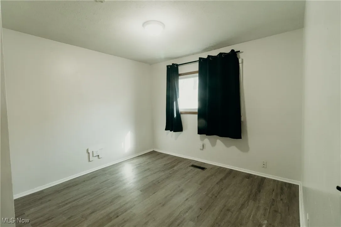 Spare room featuring dark wood-type flooring and baseboards