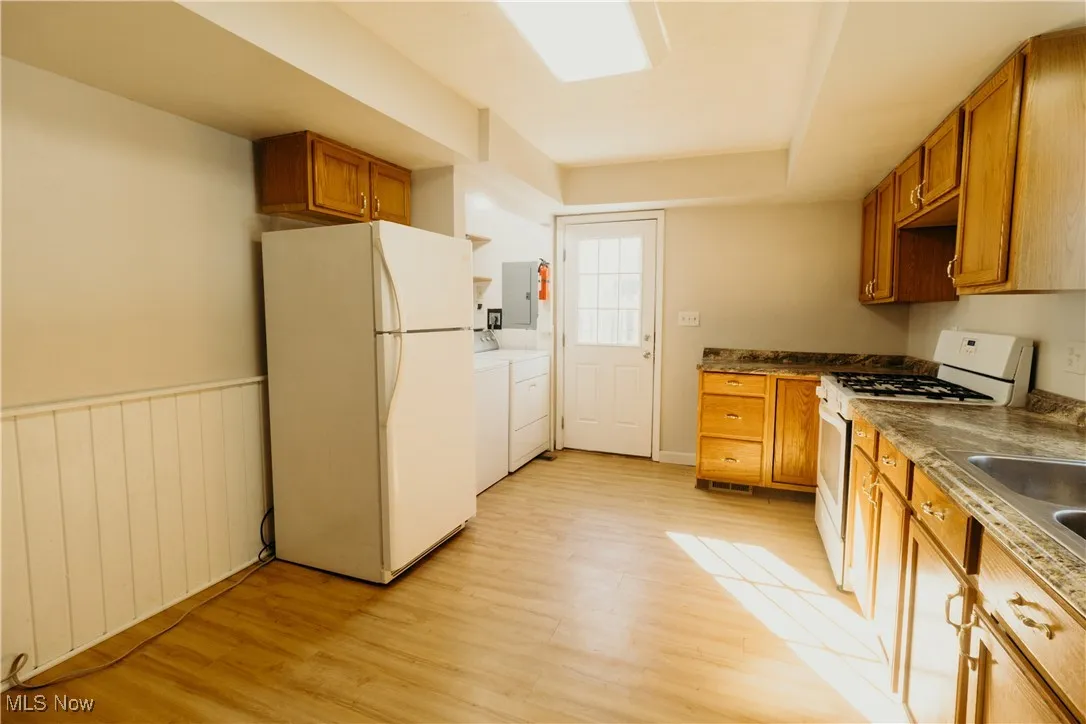 Kitchen featuring white appliances, brown cabinets, washer and clothes dryer, light wood finished floors, and electric panel