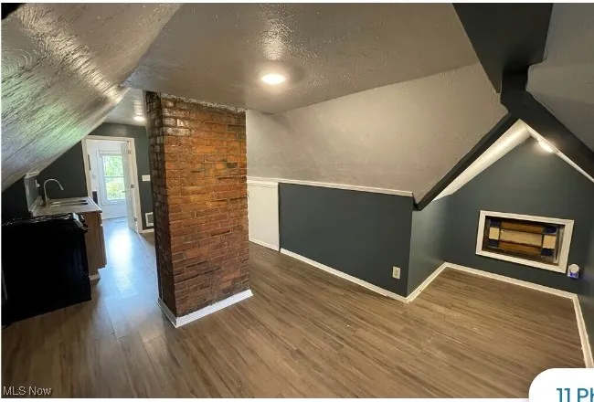 Bonus room with a textured ceiling, vaulted ceiling, and dark wood-type flooring