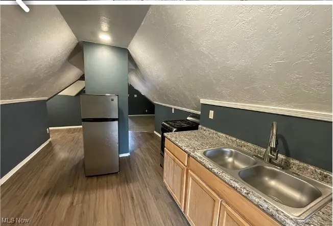 Kitchen featuring light brown cabinetry, dark wood-type flooring, freestanding refrigerator, gas range oven, and a textured ceiling